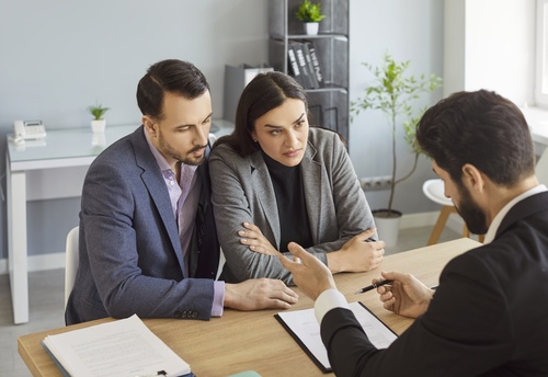 Frustrated couple sitting together with worried expressions, woman covering face with hand