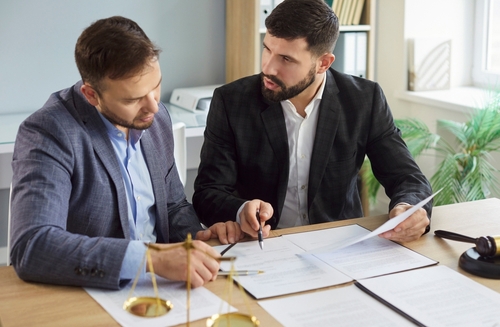 Two men in suits reviewing documents at desk with justice scales